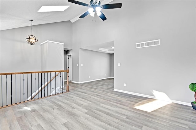 spare room featuring wood finished floors, visible vents, baseboards, a skylight, and ceiling fan with notable chandelier