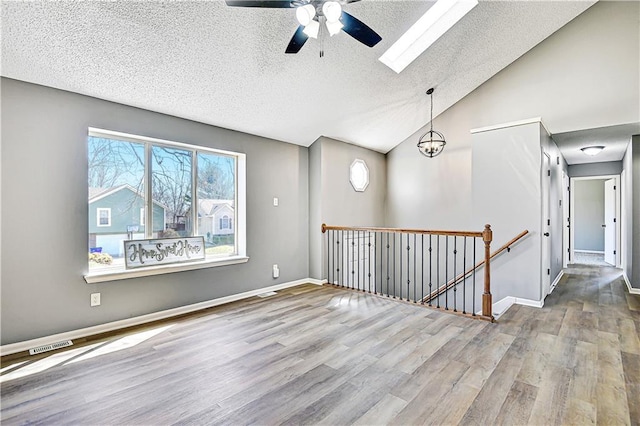 empty room with baseboards, ceiling fan, lofted ceiling with skylight, wood finished floors, and a textured ceiling