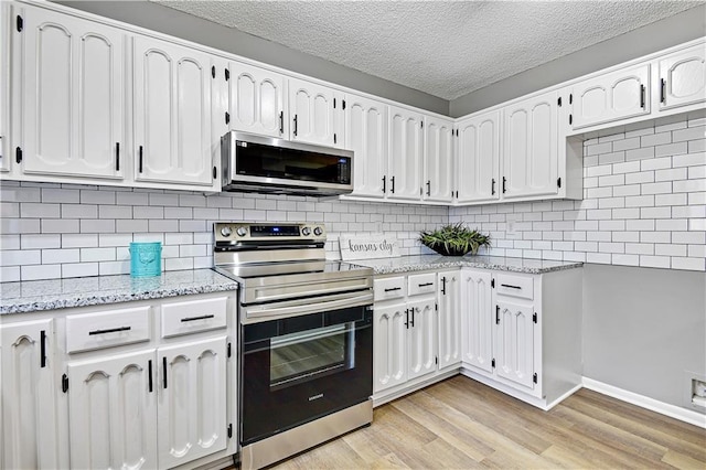 kitchen featuring light stone counters, tasteful backsplash, white cabinetry, light wood-style floors, and appliances with stainless steel finishes