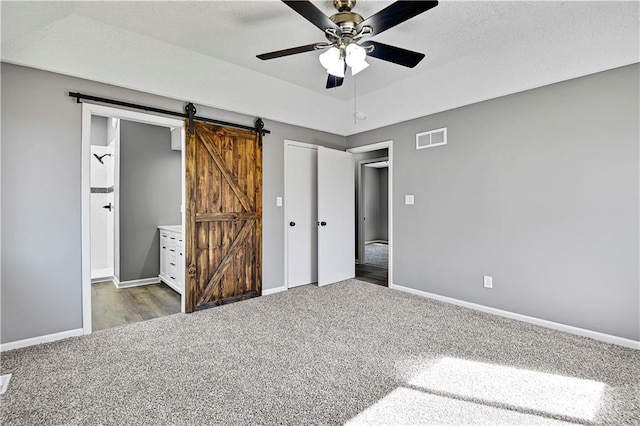 unfurnished bedroom featuring a barn door, carpet flooring, baseboards, and visible vents