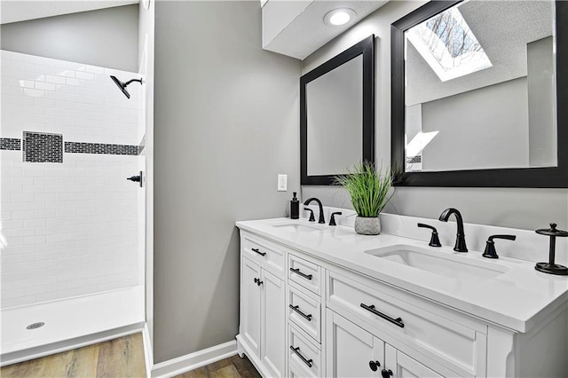 full bathroom featuring a tile shower, wood finished floors, a skylight, and a sink