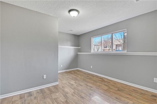 empty room with baseboards, a textured ceiling, and wood finished floors