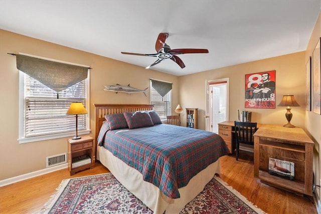 bedroom with ceiling fan, visible vents, baseboards, and wood finished floors