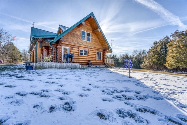 snow covered rear of property with log exterior and metal roof