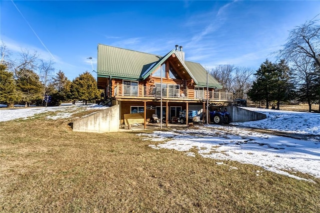 snow covered property featuring metal roof, a lawn, a wooden deck, and a chimney