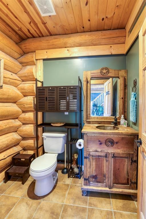 half bathroom with log walls, toilet, visible vents, and wooden ceiling