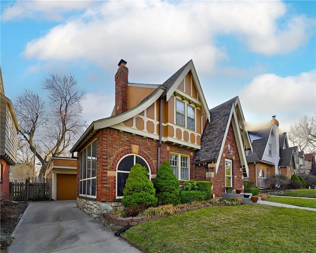 tudor-style house with a front yard, fence, stucco siding, a chimney, and brick siding