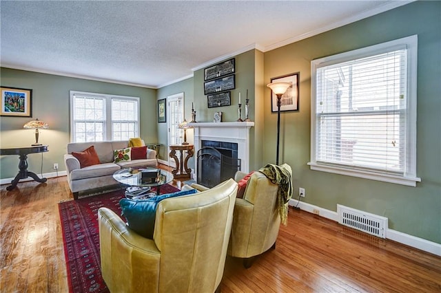 living room with wood finished floors, visible vents, baseboards, a fireplace, and crown molding