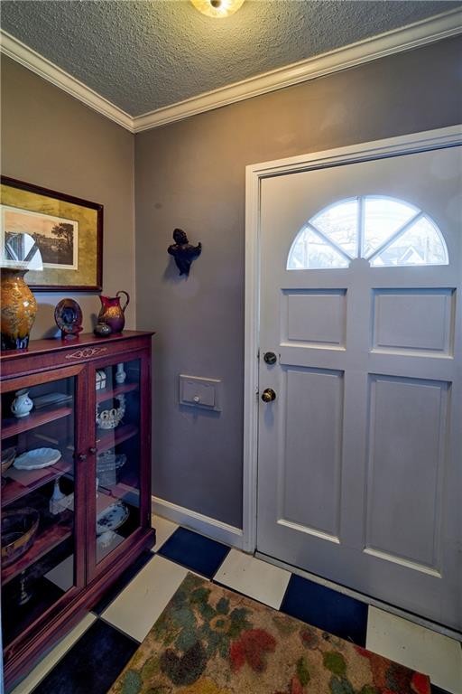 foyer entrance featuring tile patterned floors, baseboards, a textured ceiling, and ornamental molding