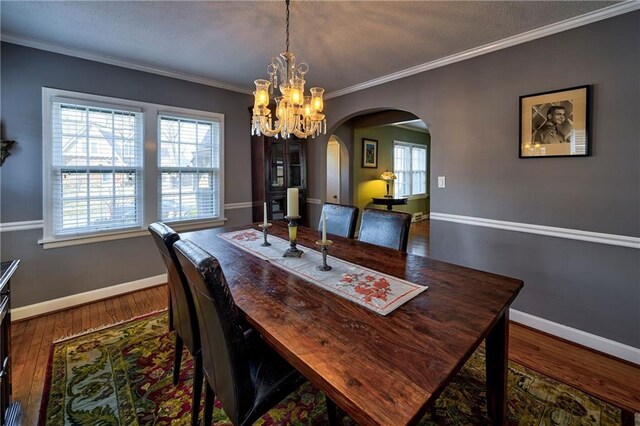 dining space featuring baseboards, arched walkways, dark wood finished floors, and ornamental molding