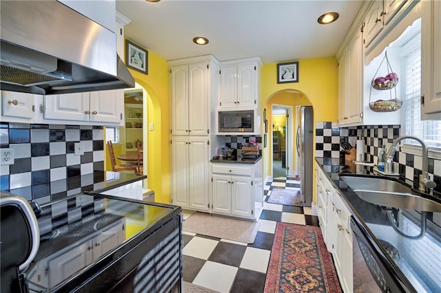 kitchen with a sink, arched walkways, extractor fan, and appliances with stainless steel finishes