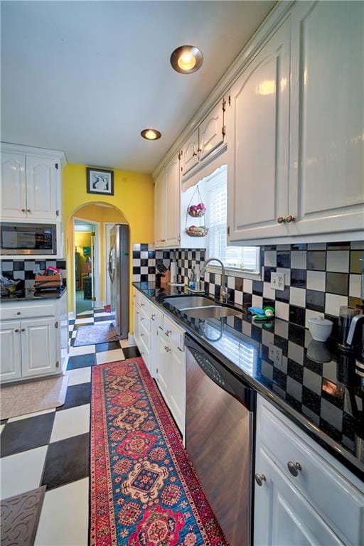 kitchen featuring a sink, arched walkways, appliances with stainless steel finishes, white cabinets, and light floors