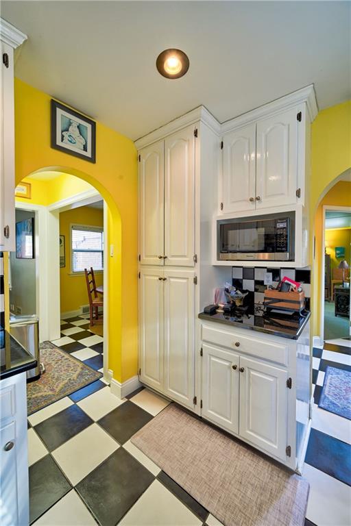 kitchen featuring light floors, dark countertops, arched walkways, white cabinets, and stainless steel microwave