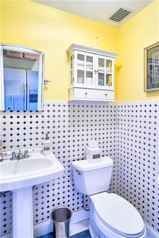 bathroom with a wainscoted wall, tile walls, toilet, and visible vents