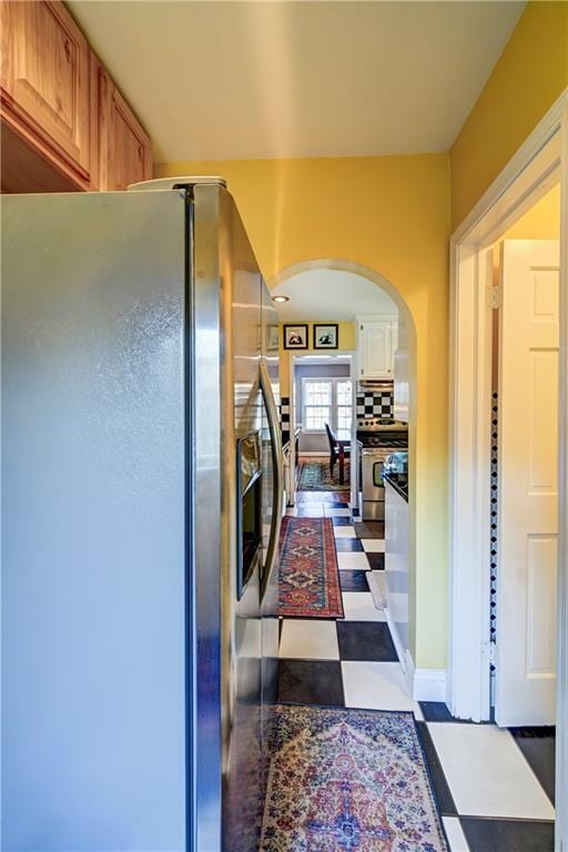 kitchen featuring backsplash, brown cabinetry, arched walkways, tile patterned floors, and stainless steel appliances