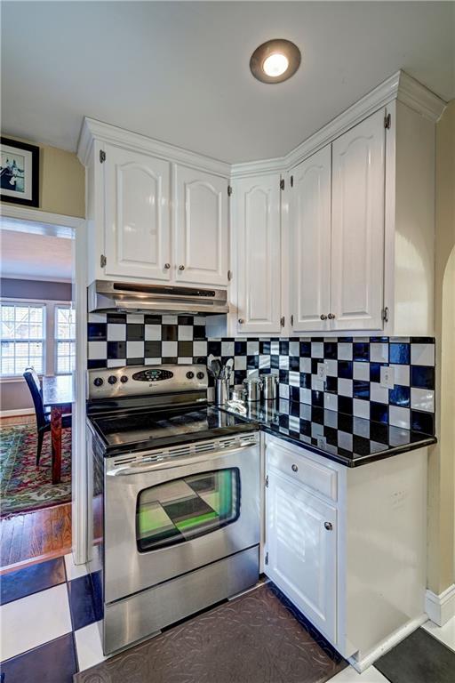 kitchen featuring dark countertops, tasteful backsplash, under cabinet range hood, stainless steel range with electric stovetop, and white cabinetry