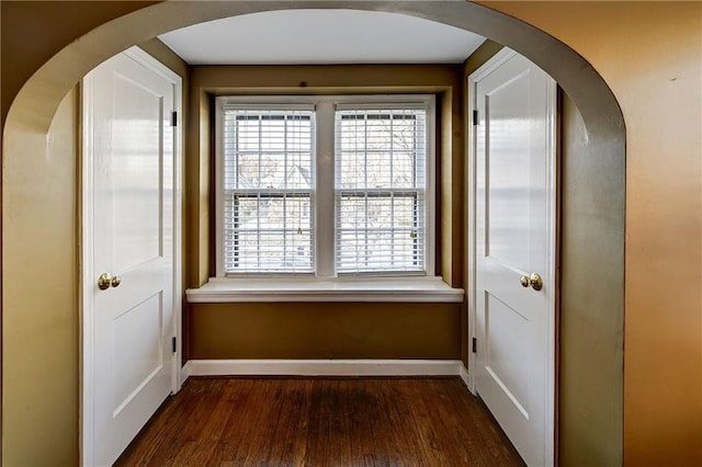 corridor featuring baseboards, arched walkways, and dark wood finished floors