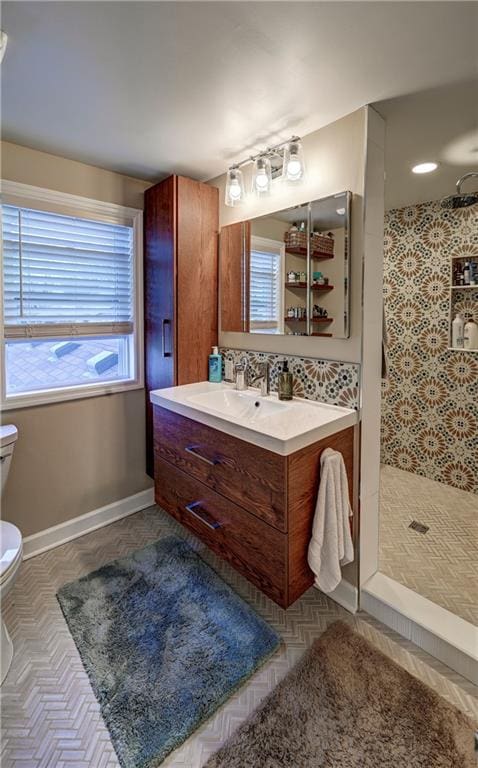 full bathroom featuring tiled shower, toilet, vanity, and baseboards