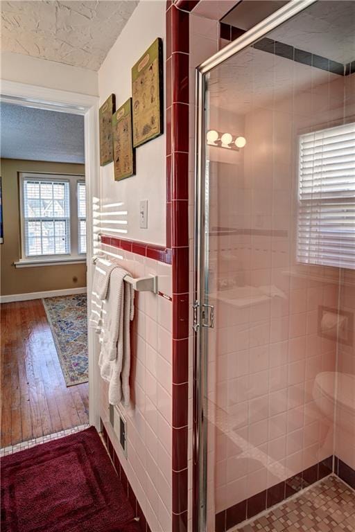 full bathroom featuring a stall shower, tile walls, a textured ceiling, and wood finished floors