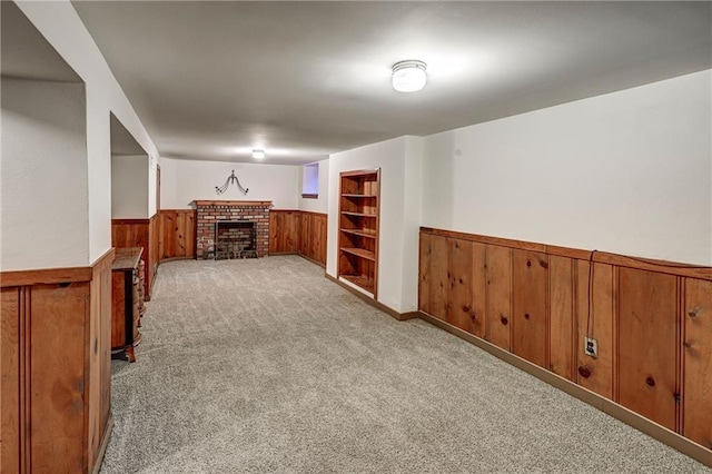 finished basement with wooden walls, built in shelves, a wainscoted wall, carpet floors, and a fireplace