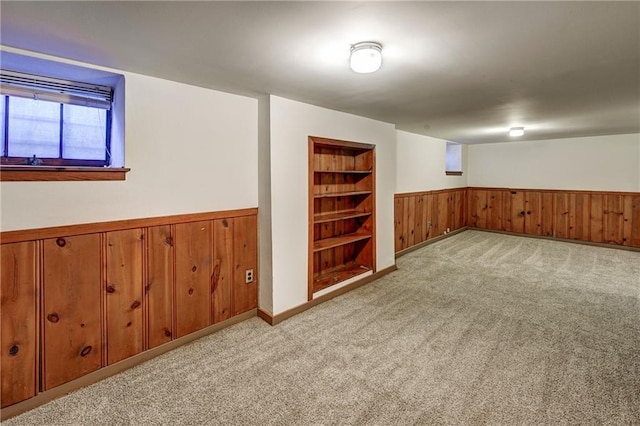 below grade area featuring built in shelves, carpet, a wainscoted wall, and wood walls