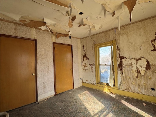 empty room featuring crown molding, dark floors, and wallpapered walls