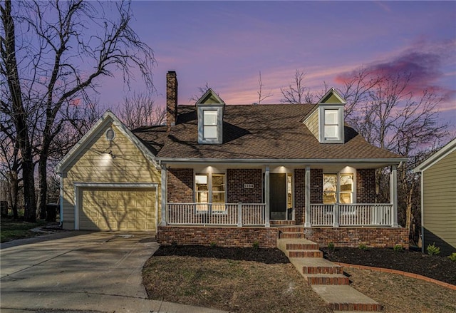 new england style home with driveway, covered porch, a garage, brick siding, and a chimney