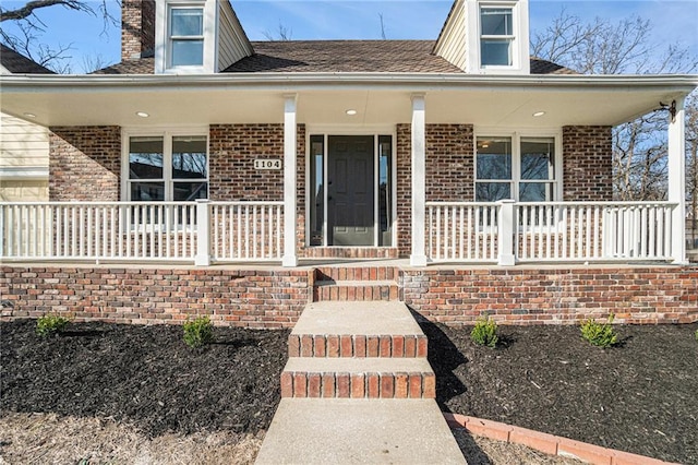 view of exterior entry featuring brick siding and covered porch