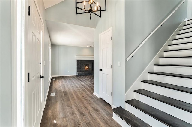 interior space with a notable chandelier, wood finished floors, stairway, baseboards, and a brick fireplace