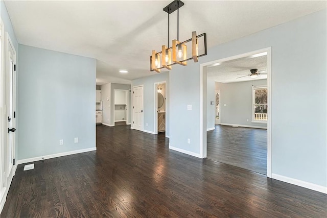 empty room featuring ceiling fan with notable chandelier, a textured ceiling, baseboards, and dark wood-style flooring