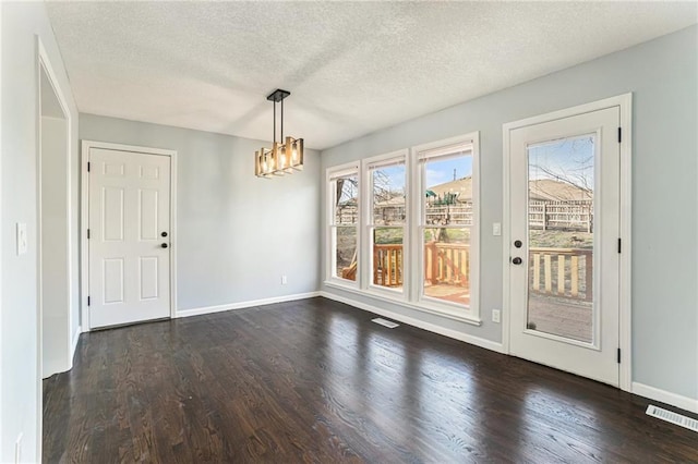 unfurnished dining area featuring visible vents, a textured ceiling, baseboards, a chandelier, and dark wood-style flooring