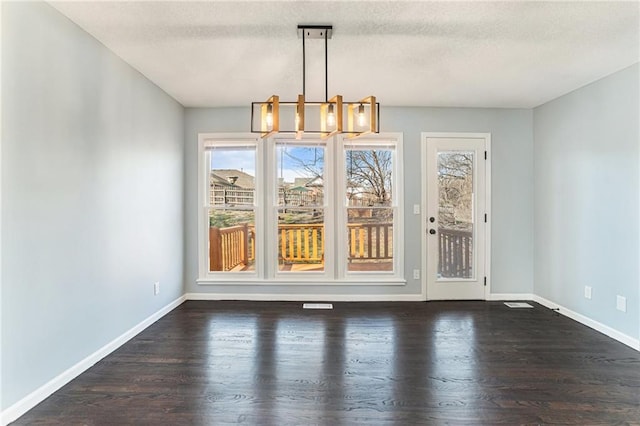 unfurnished dining area featuring dark wood-style floors, a notable chandelier, a textured ceiling, and baseboards