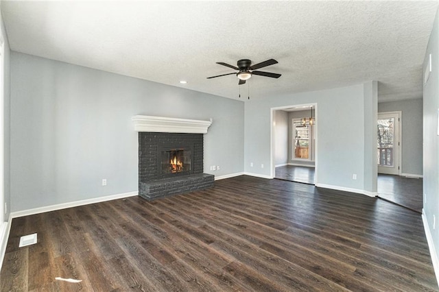 unfurnished living room featuring ceiling fan with notable chandelier, a textured ceiling, dark wood-style floors, a fireplace, and baseboards