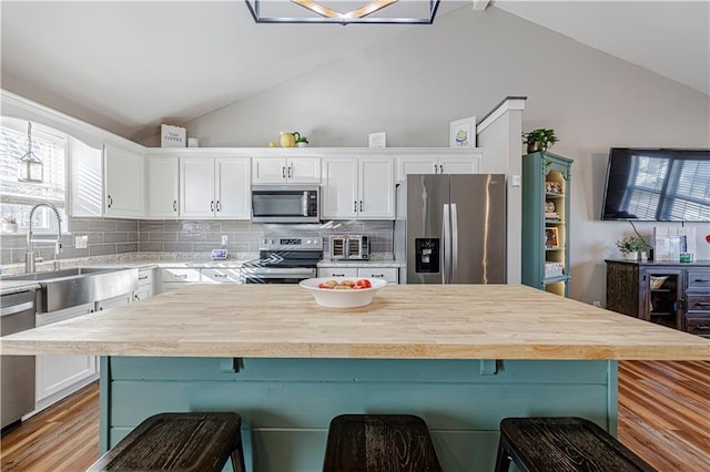 kitchen with a sink, white cabinetry, appliances with stainless steel finishes, light countertops, and lofted ceiling