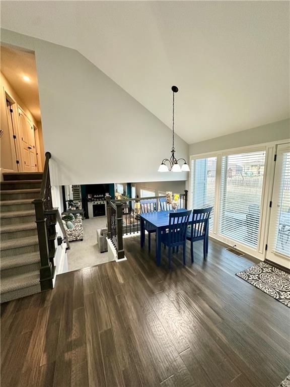 dining area with dark wood-style floors, high vaulted ceiling, an inviting chandelier, a fireplace, and stairs