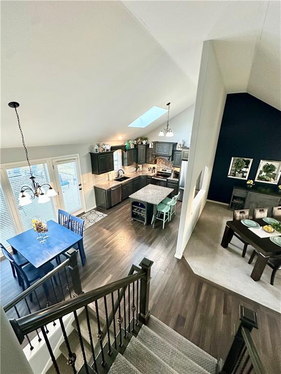 staircase featuring wood finished floors, a chandelier, and vaulted ceiling with skylight