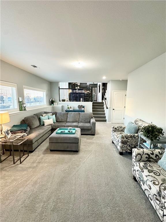 living room featuring visible vents, carpet flooring, and stairway