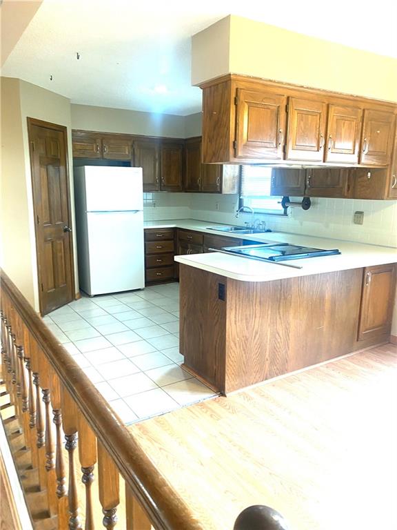 kitchen featuring a peninsula, freestanding refrigerator, a sink, light countertops, and tasteful backsplash