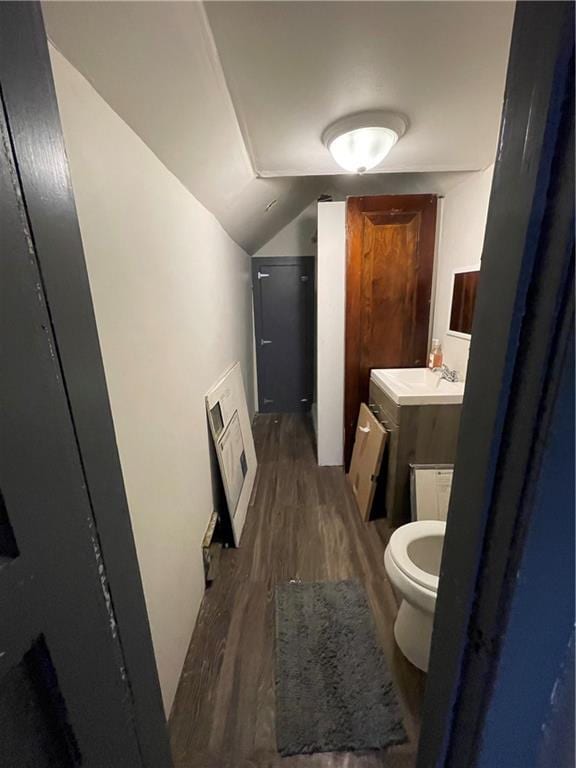 half bathroom featuring vaulted ceiling, toilet, vanity, and wood finished floors