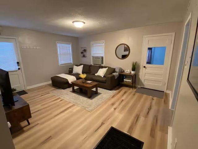 living room featuring cooling unit, baseboards, and light wood-style floors