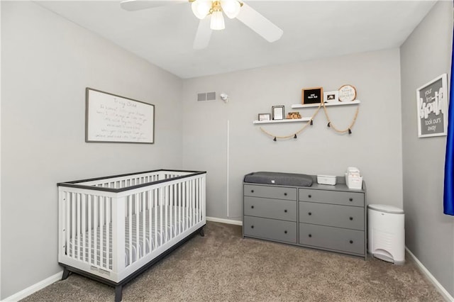 carpeted bedroom with visible vents, baseboards, a nursery area, and ceiling fan