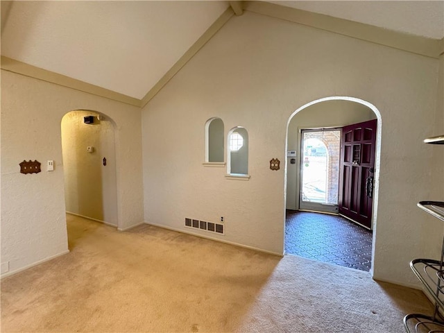 entrance foyer with beamed ceiling, arched walkways, visible vents, and a textured wall