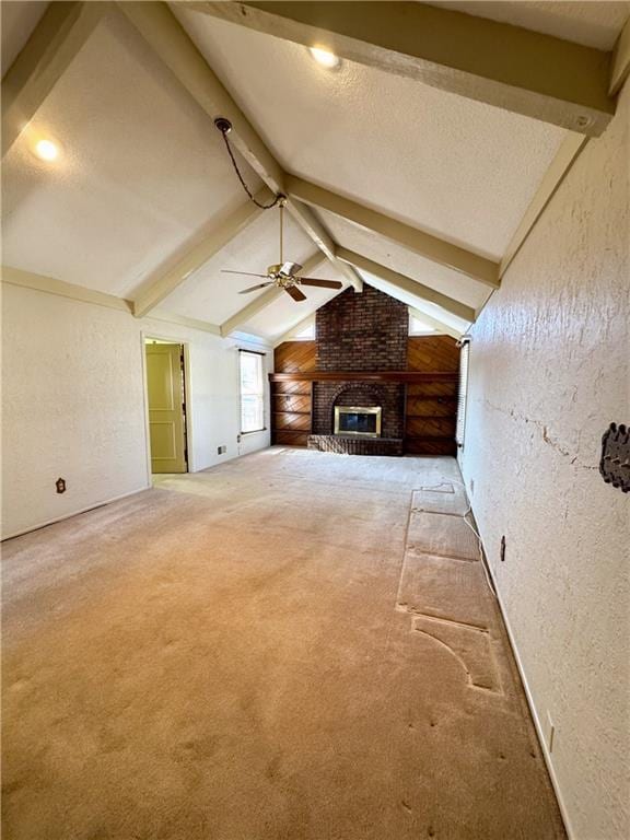 unfurnished living room featuring lofted ceiling with beams, ceiling fan, a fireplace, and a textured wall