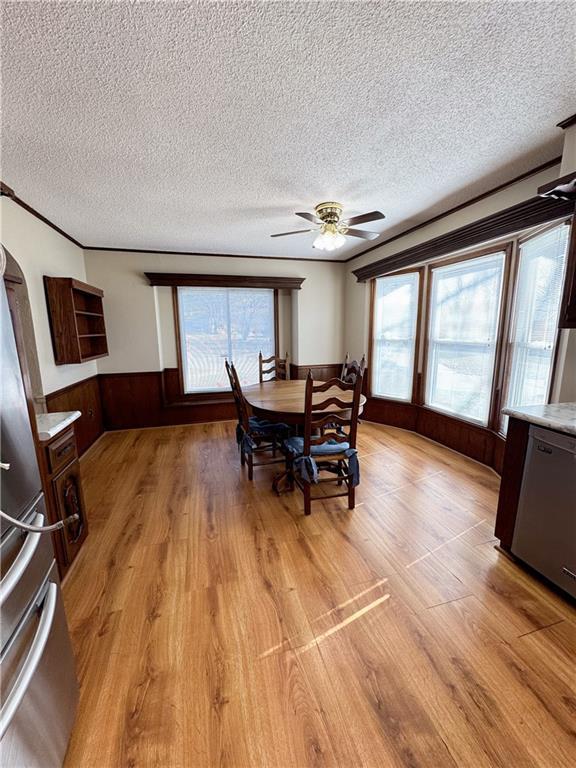 dining area featuring crown molding, ceiling fan, a wainscoted wall, light wood-type flooring, and a textured ceiling