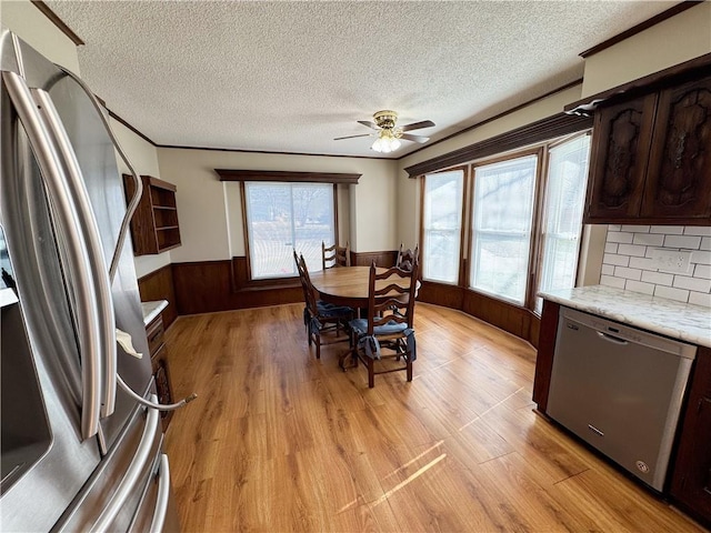 dining room featuring wainscoting, ceiling fan, wood walls, a textured ceiling, and light wood-type flooring