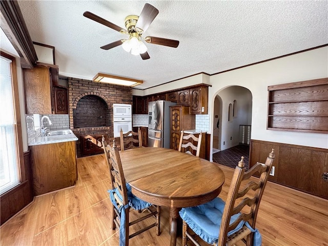 dining space featuring light wood-type flooring, ornamental molding, arched walkways, wainscoting, and ceiling fan