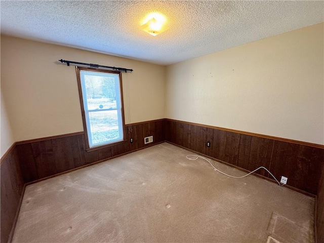 carpeted empty room featuring visible vents, wooden walls, wainscoting, and a textured ceiling