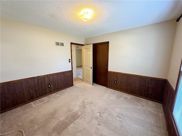 empty room with a wainscoted wall, visible vents, and wood walls