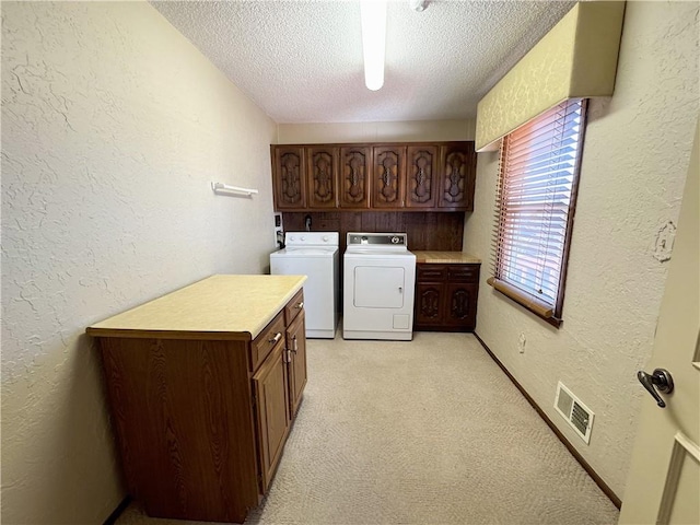 clothes washing area with washer and clothes dryer, visible vents, cabinet space, and a textured wall