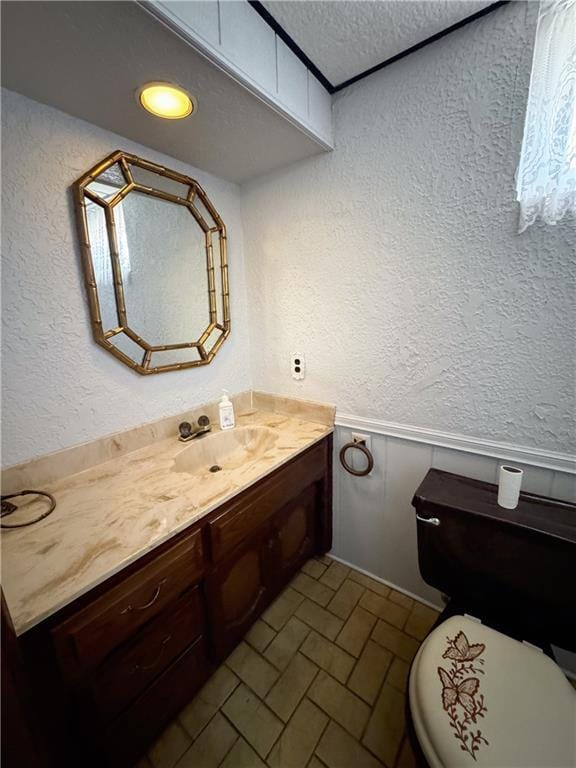 half bathroom with toilet, brick patterned floor, vanity, and a textured wall